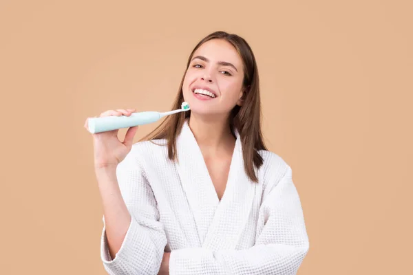 Young woman brushing teeth. Happy funny girl brush her teeth on isolated background. Beautiful wide smile of young woman with great healthy white teeth on beige background
