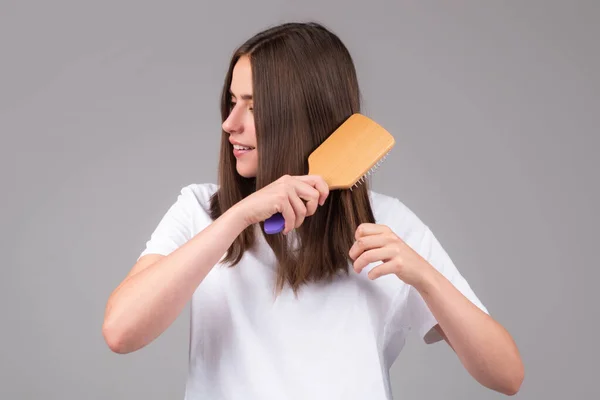 Brushing Hair. Portrait young woman brushing straight natural hair with comb. Girl combing veautiful long healthy hair with hairbrush. Hair care beauty concept