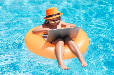 Konseptin dışında çalış. Çocuk havuzda rahatlıyor, yaz suyunda dizüstü bilgisayar kullanıyor. Çocuk çevrimiçi çalışması ya da tropikal deniz sahillerinde çalışmak. Yaşam konsepti teknolojisi