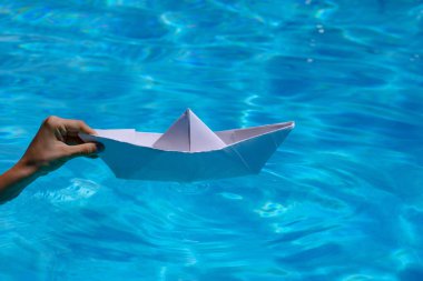 El, açık deniz suyuna beyaz kağıt bir tekne fırlatıyor. Origami kağıt tekne
