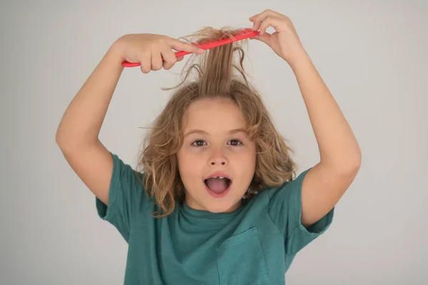 Excited child with curly blonde hair holding comb hairbrush for combing. Child with tangled blonde long hair tries to comb it. Hair portrait kid with a comb