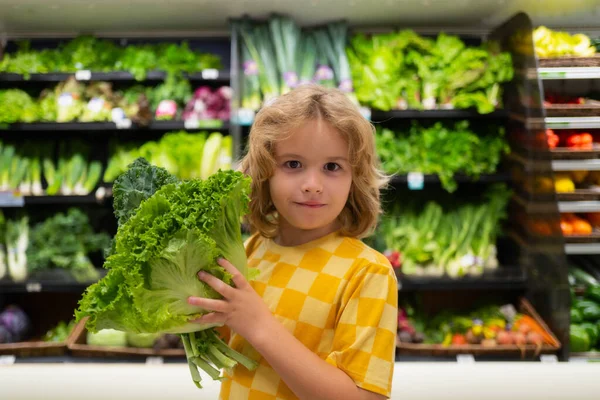 Child with lettuce chard vegetables. Funny cute child on shopping in supermarket. Grocery store. Grocery shopping, healthy lifestyle concept