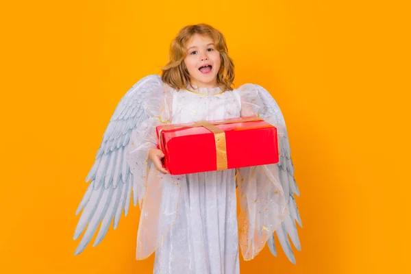 Angel with gift box present. Child angel. Portrait of cute kid with angel wings isolated on yellow studio background. Little angel, valentines day. Angelic kids