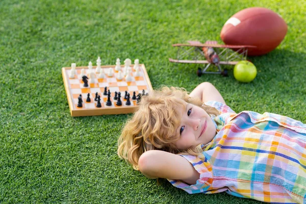 Chess school outdoor. Child laying on grass in spring park and think about chess game. Child education concept. Intelligent and clever school kids. Kid relax in park, laying on grass, daydreaming