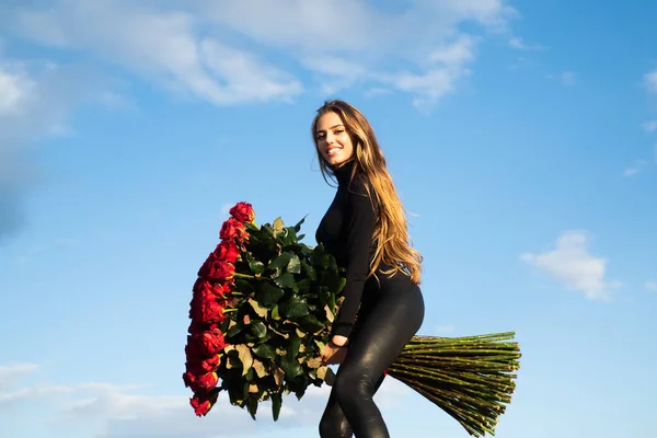 Large bouquet of roses. Sexy woman posing near roses on sky background. Sensual woman in rose garden. Elegant lady posing with big roses bouquet