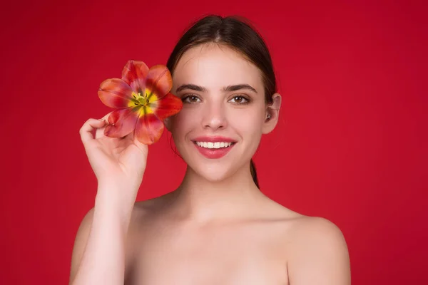 漂亮的女孩 脸上有郁金香 青年和皮肤护理概念 美丽的性感女人拿着郁金香 红色背景的工作室肖像 — 图库照片
