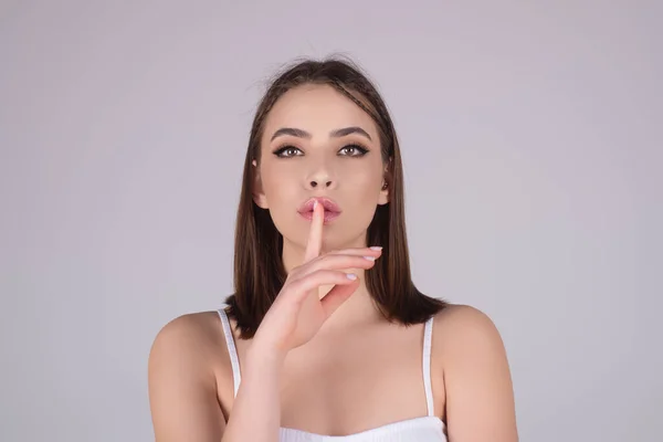 Beauty and silence concept. Portrait of attractive funny young lady showing shhh taboo sign with finger to lips over studio background, isolated. Shhh sign, facial expression, secret