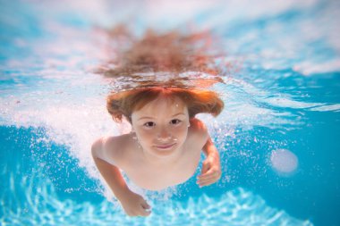 Young boy swim and dive underwater. Under water portrait in swim pool. Child boy diving into a swimming pool. Water play, healthy outdoor sport activity for children