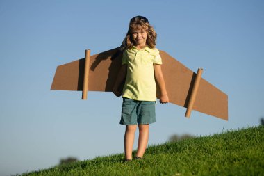 Pilot olacak çocuk. Kağıt kanatlı çocuk uçuyor. Yaz tatili ve seyahat konsepti. Oyuncak karton uçak kanatlarıyla gökyüzünde uçan komik çocuk. Çocuklar yazın doğada seyahat etmeyi hayal ederler.