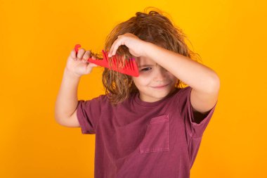 Funny hairstyle. Child with tangled blonde long hair tries to comb it. Hair portrait kid with a comb