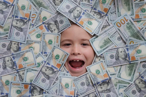 Funny child with fun face with money. Kid peeking out of dollar bills with astonished shocked eyes. Money background. Money banknotes, cash dollars bills