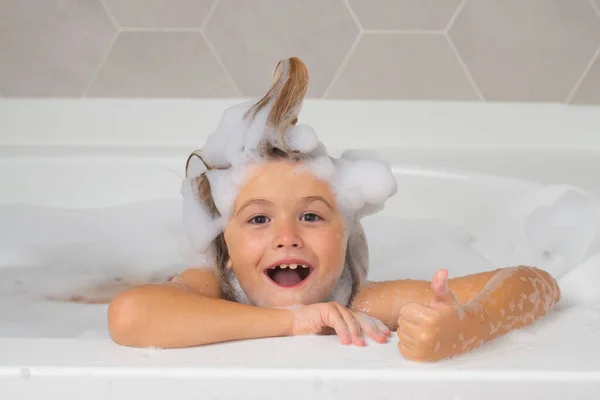 Kid in a bath tub. Washing in bath with soap suds on hair. Child taking bath. Closeup portrait of smiling kid, health care and kids hygiene. Kids face in bath tub with foam