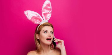Tavşanlı Paskalya bayrağı. Paskalya tavşanı. Pembe arka planda izole edilmiş cep telefonlu genç bir kadın.