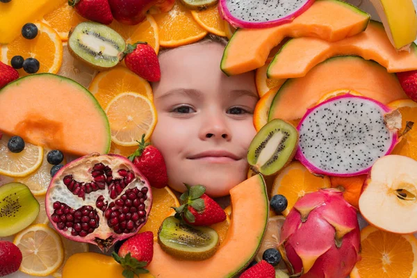 Funny child eats organic fruits. Healthy meal nutrition for children. Child eat tasty fruits. Fresh fruit and child face top view. Mix of raw fresh fruits