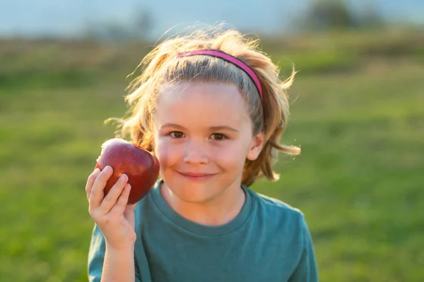 Apple child. Child bites big apple, against green summer garden