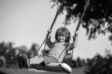 Arka bahçede çocuk salıncağı. Çocuk dışarıda oynuyor. Mutlu küçük çocuk sallanıyor ve sağlıklı yaz tatili aktiviteleri yapıyor.