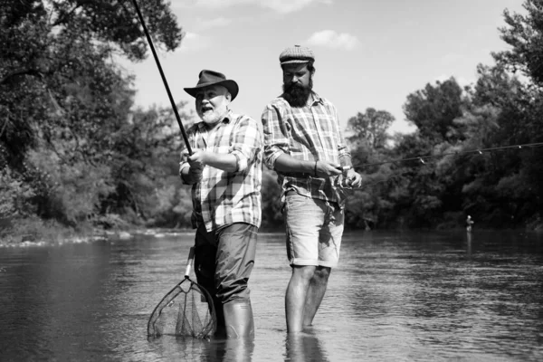 Bearded elegant men. Fisher fishing equipment. Fishing is fun. Man relaxing and fishing by lakeside. Pothunter. Fly fish hobby of men in checkered shirt. Brutal man stand in river water
