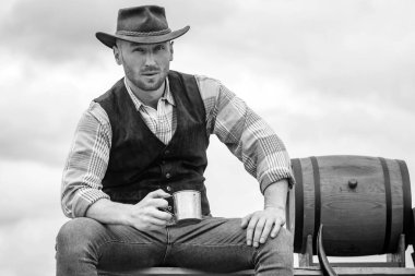 Yakışıklı sakallı maço adam. Erkeklerin güzellik standardı. Gerçek erkekliğin bir örneği. Şapkalı bir kovboy. Batı hayatı. Tıraşsız kovboy şapkalı ve ekose gömlekli adam alkol içiyor.