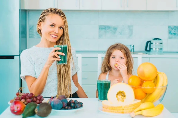 Little daughter and her happy mother drinks green smoothie. Natural antioxidant. Healthy Green food. Mother and daughter with glass of natural detox smoothie in kitchen. Perfect energy and calorie