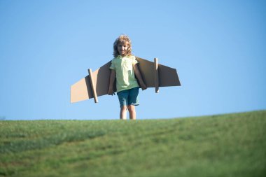 Komik çocuk dışarıda uçak kanatlarıyla oynuyor. Pilotçuluk oynayıp pilot olmanın hayalini kuran sevimli çocuk. Dışarıda kağıt kanatlarla eğlenen bir çocuk. Yaz tatili ve çocukların seyahat konsepti