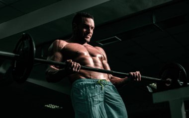 Halter kaldıran formda bir adam. Spor salonunda egzersiz yapan kaslı bir adam. Güçlü erkek, çıplak karın kasları.