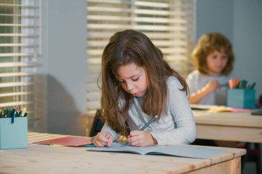Okul sınıfında masada oturan sevimli bir kızın portresi. Öğrenci çizimleri, anaokulu çocuk çalışmaları. Çocuk eğitimi, evde eğitim kavramı