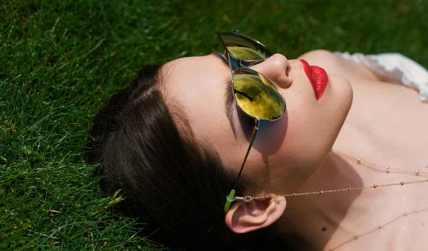 Spring woman face for banner. Elegant chic female model in fashion sunglasses. Beautiful young brunette with perfect skin and long dark hair. Grass background