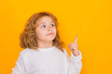 Child pointing up on yellow isolated studio background. Shocked kid pointing to copyspace, showing promo offers, points up