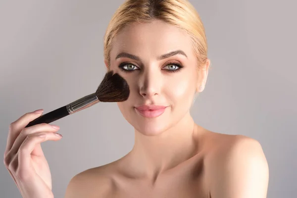 Beautiful young woman apply powder on face. Beauty Makeup. Portrait of female model with cosmetic brush. Perfect soft skin and natural makeup. Applying powder blush highlighter, foundation tone