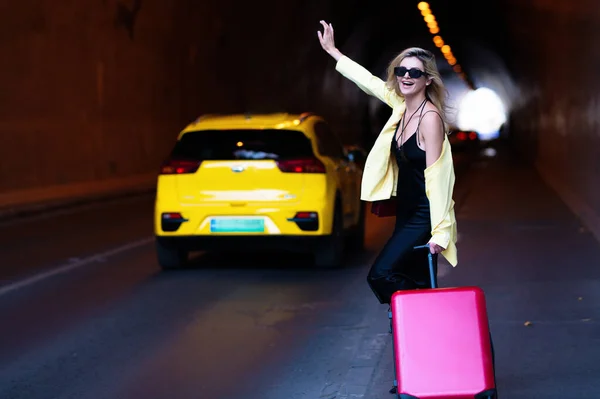Woman with a suitcase take taxi. Yellow taxi. Travelling concept. Sexy young woman on trip walking with his luggage on street. Sensual girl with travel bag ready to travel on vacation