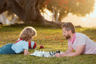 Father and son playing chess spending time together outdoor. Games and entertainment for children. Family concept