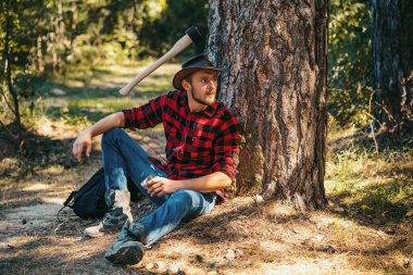 Ormanın yakınında baltası olan yakışıklı bir genç. Oduncu ormanda oturuyor.