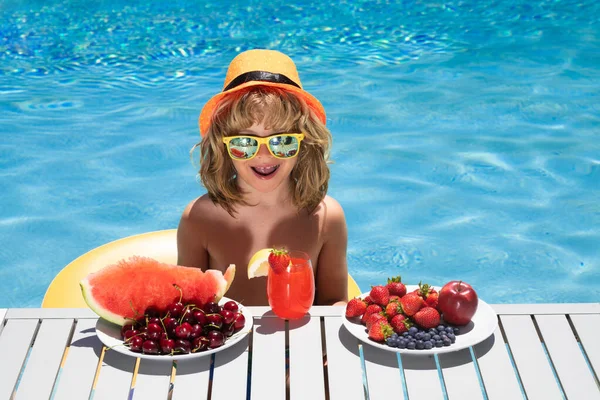 Summer excited child by the pool eating fruit and drinking lemonade cocktail. Summer kids. Little kid boy relaxing in a pool having fun during summer vacation. Funny amazed kids face