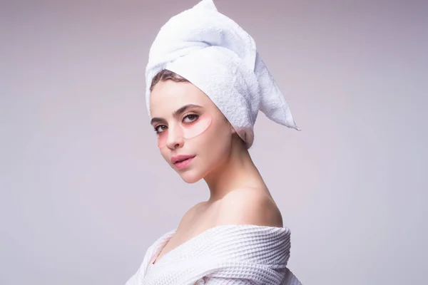 Woman applying eye patches. Close up portrait girl with towel on head and patches under eyes. Portrait of beauty woman with eye patches and perfect skin. Morning skincare routine