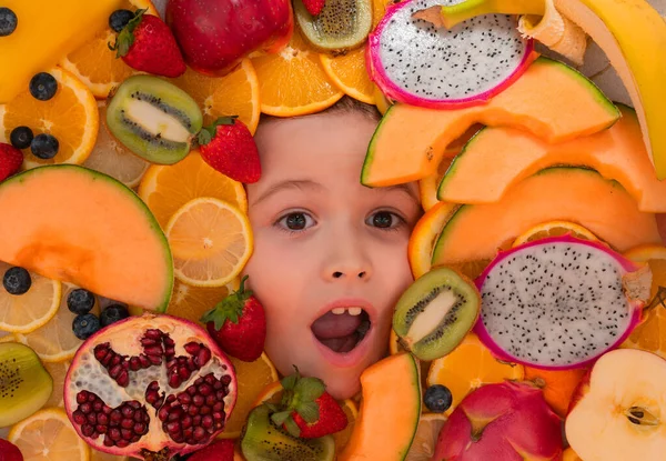 Kid tasting fruits. Funny fruits. Surprised kids face with mix of strawberry, blueberry, strawberry, kiwi, dragon fruit, pomegranate, orange and melon. Assorted mix of fruits near child face