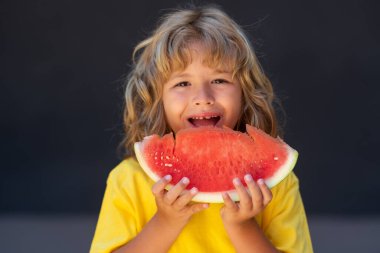 Kid face and watermelon, close up. Child eat watermelon. Kid is picking watermelon on gray background