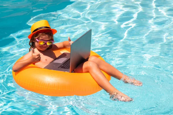 Kids working with laptop on summer vacation holidays. Little freelancer using computer, remote working in swimming pool