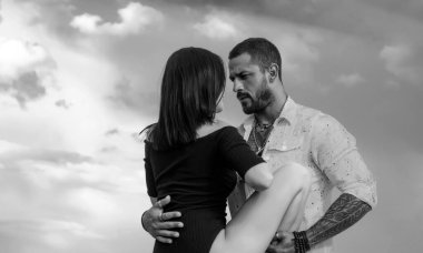 Gökyüzüne karşı güzel bir çift. Çiftler dışarıda romantik bir yürüyüş yapar. Gerçek aşk konsepti. Duygusal bir kadın dramatik gri arka planda vahşi bir adama bacağını kaldırıyor.