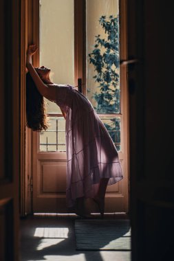 Uzun saçlı güzel bir kız. O mutlu dans eder. Kız gece kıyafeti giymiş. Balkonun yanında duran genç bir kadın. Seksi iç çamaşırlı manken.