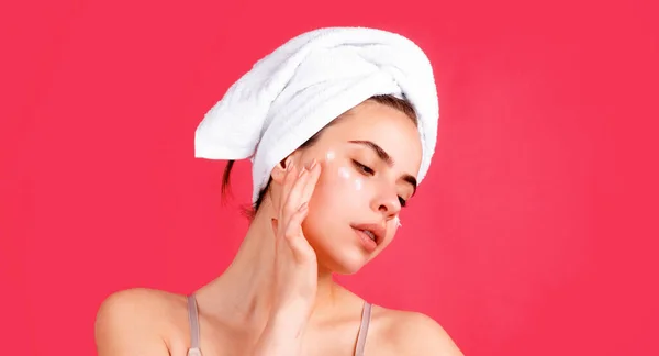 Cosmetic cream on woman face with clean soft skin. Woman with towel applying cream on skin. Body care and spa salon concept. Spa sensual girl. Beautiful young woman with perfect skin