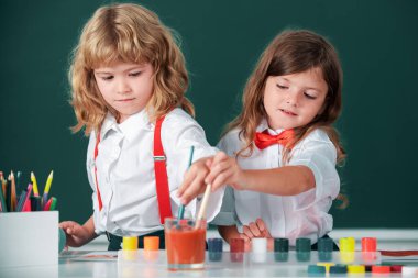 Sınıfta karatahta arka planda komik öğrenciler çiziyor. Okul arkadaşları çocuklar, kız ve erkek birlikte resim yapıyorlar. Çocukluk eğitimi, çocukların sanatsal becerileri.