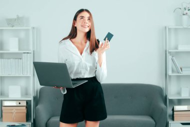 Dizüstü bilgisayarı ve kredi kartı olan genç bir iş kadını ofiste çok fazla işi olan bir bilgisayarla çalışıyor. Sekreter kız