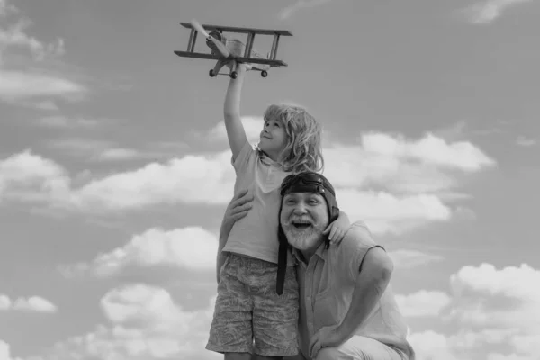 Grandfather and son with toy jetpack plane against sky. Child pilot aviator with plane dreams of traveling