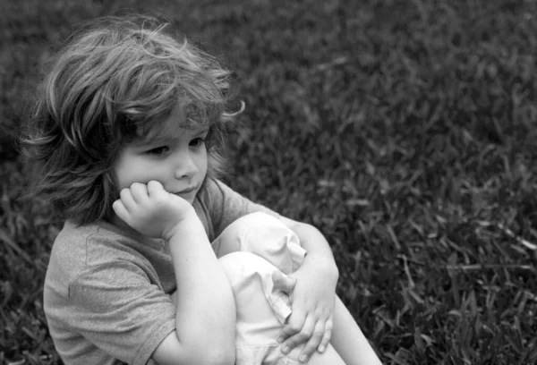 Its sad. Little child sad boy sit in grass, summer. Childhood, youth, growth
