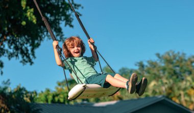 Çocuk dışarıda sallanıyor. Çocuk arka bahçede oynuyor. Mutlu küçük çocuk sallanıyor ve sağlıklı yaz tatili aktiviteleri yapıyor.