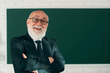 Komik kıdemli profesör. Kollarını kavuşturup tahtaya yaslanmış mutlu son sınıf öğretmeninin portresi.