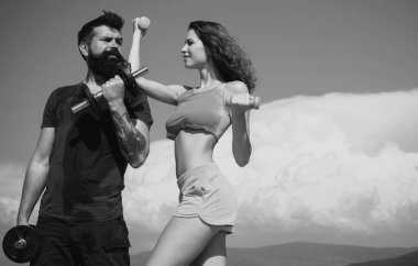 Çekici genç çift boş vakitlerinde fitness egzersizleri yapıyor. Güzel esmer kadın ve sakallı yakışıklı adam mavi gökyüzü arka planında spor fitness aktiviteleri yapıyorlar.