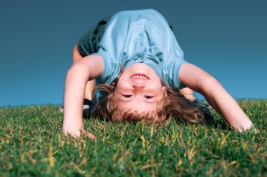 Dışarıdaki çimlerin üzerinde baş aşağı oynayan mutlu bir çocuğun portresi. Gülen çocuk. Etkileyici yüz ifadeleri.