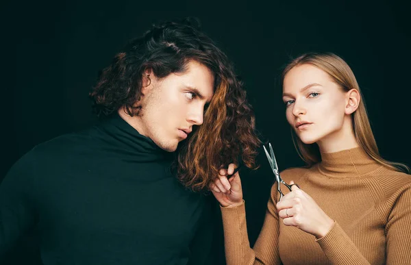 Hairdresser girl going to cut off long wavy bleached dry hair of customer man. Man hair style, wellness and fashion. Female with scissors going to do amazing man haircut. Hair salon concept
