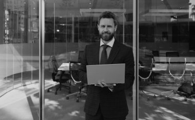 İş adamının elinde dizüstü bilgisayar vardı. İş yerinin yakınında duruyordu.